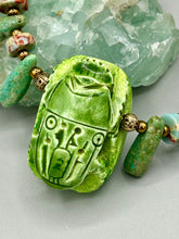 Load image into Gallery viewer, This powerful statement piece necklace features an eye-catching hand sculpted dark blue clay scarab beetle pendant. Adorned with green magnesite and serpentine teintee stone beaded necklace, this dramatic necklace artfully wraps around the neck, conveying an elegant and bold style. Necklace is 20 1/4" in length