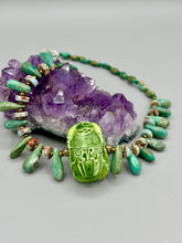Load image into Gallery viewer, This powerful statement piece necklace features an eye-catching hand sculpted dark blue clay scarab beetle pendant. Adorned with green magnesite and serpentine teintee stone beaded necklace, this dramatic necklace artfully wraps around the neck, conveying an elegant and bold style. Necklace is 20 1/4" in length