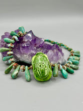 Load image into Gallery viewer, This powerful statement piece necklace features an eye-catching hand sculpted dark blue clay scarab beetle pendant. Adorned with green magnesite and serpentine teintee stone beaded necklace, this dramatic necklace artfully wraps around the neck, conveying an elegant and bold style. Necklace is 20 1/4" in length