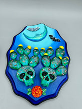 Load image into Gallery viewer, This carefully crafted polymer clay wall art showcases a wood frame adorned with a crescent moon motif. A striking color palette of deep sky tones, including light blue and royal blue to black, further enhances the piece. Delicate cacti plants bloom with light yellow flowers, with spooky skulls are incorporated among the cacti plant and a finishing touch of flying bat motifs. Measurements: H 9" x W 6 1/2” x D 1 1/4"