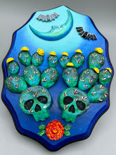 Load image into Gallery viewer, This carefully crafted polymer clay wall art showcases a wood frame adorned with a crescent moon motif. A striking color palette of deep sky tones, including light blue and royal blue to black, further enhances the piece. Delicate cacti plants bloom with light yellow flowers, with spooky skulls are incorporated among the cacti plant and a finishing touch of flying bat motifs. Measurements: H 9" x W 6 1/2” x D 1 1/4"