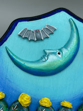 Load image into Gallery viewer, This carefully crafted polymer clay wall art showcases a wood frame adorned with a crescent moon motif. A striking color palette of deep sky tones, including light blue and royal blue to black, further enhances the piece. Delicate cacti plants bloom with light yellow flowers, with spooky skulls are incorporated among the cacti plant and a finishing touch of flying bat motifs. Measurements: H 9" x W 6 1/2” x D 1 1/4"