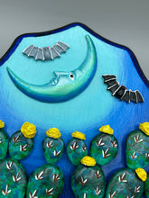 Load image into Gallery viewer, This carefully crafted polymer clay wall art showcases a wood frame adorned with a crescent moon motif. A striking color palette of deep sky tones, including light blue and royal blue to black, further enhances the piece. Delicate cacti plants bloom with light yellow flowers, with spooky skulls are incorporated among the cacti plant and a finishing touch of flying bat motifs. Measurements: H 9" x W 6 1/2” x D 1 1/4"