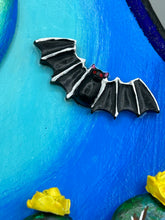Load image into Gallery viewer, This carefully crafted polymer clay wall art showcases a wood frame adorned with a crescent moon motif. A striking color palette of deep sky tones, including light blue and royal blue to black, further enhances the piece. Delicate cacti plants bloom with light yellow flowers, with spooky skulls are incorporated among the cacti plant and a finishing touch of flying bat motifs. Measurements: H 9" x W 6 1/2” x D 1 1/4"