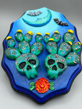 Load image into Gallery viewer, This carefully crafted polymer clay wall art showcases a wood frame adorned with a crescent moon motif. A striking color palette of deep sky tones, including light blue and royal blue to black, further enhances the piece. Delicate cacti plants bloom with light yellow flowers, with spooky skulls are incorporated among the cacti plant and a finishing touch of flying bat motifs. Measurements: H 9" x W 6 1/2” x D 1 1/4"