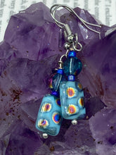 Load image into Gallery viewer, This set of glass beaded earrings features a vibrant blue shade with hints of purples and gold for an overall dynamic look. Its unique texture is derived from the combination of different size and shaped beads, resulting in a bold, eye-catching piece. For any discerning connoisseur, this set is a must-have addition to any jewelry collection.  Measurements: 1 1/2” in length