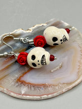 Load image into Gallery viewer, Peruvian off white ceramic skull beads come with quartzite red rose beads. These stylish skull earrings are perfect for adding a unique flair to any outfit. Whether you're looking for a Dia De Los Muertos accessory or simply looking to draw inspiration, these goth pieces perfectly capture the vampire goth, witchy, dark, Chingona Cabrona, Latina Chicana styles. Measurements: 1” in length