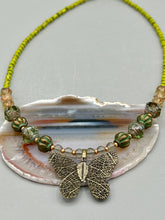 Load image into Gallery viewer, This intricately crafted pendant features a basil leaf molded in brass and adorned with stunningly warm greens, blues, and gold tone beaded necklace. Its eye-catching butterfly design adds a bold, yet whimsical touch, making it an ideal choice for a summer look. This beaded necklace is crafted from a combination of brass floral beads with a subtle patina hue, champagne melon beads, and dark, faceted avocado green pressed glass beads.  Measurements: Necklace is 18 1/2” in length - pendant is 1” Height