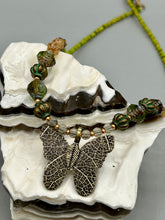 Load image into Gallery viewer, This intricately crafted pendant features a basil leaf molded in brass and adorned with stunningly warm greens, blues, and gold tone beaded necklace. Its eye-catching butterfly design adds a bold, yet whimsical touch, making it an ideal choice for a summer look. This beaded necklace is crafted from a combination of brass floral beads with a subtle patina hue, champagne melon beads, and dark, faceted avocado green pressed glass beads.  Measurements: Necklace is 18 1/2” in length - pendant is 1” Height