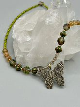 Load image into Gallery viewer, This intricately crafted pendant features a basil leaf molded in brass and adorned with stunningly warm greens, blues, and gold tone beaded necklace. Its eye-catching butterfly design adds a bold, yet whimsical touch, making it an ideal choice for a summer look. This beaded necklace is crafted from a combination of brass floral beads with a subtle patina hue, champagne melon beads, and dark, faceted avocado green pressed glass beads.  Measurements: Necklace is 18 1/2” in length - pendant is 1” Height