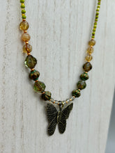 Load image into Gallery viewer, This intricately crafted pendant features a basil leaf molded in brass and adorned with stunningly warm greens, blues, and gold tone beaded necklace. Its eye-catching butterfly design adds a bold, yet whimsical touch, making it an ideal choice for a summer look. This beaded necklace is crafted from a combination of brass floral beads with a subtle patina hue, champagne melon beads, and dark, faceted avocado green pressed glass beads.  Measurements: Necklace is 18 1/2” in length - pendant is 1” Height