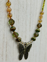 Load image into Gallery viewer, This intricately crafted pendant features a basil leaf molded in brass and adorned with stunningly warm greens, blues, and gold tone beaded necklace. Its eye-catching butterfly design adds a bold, yet whimsical touch, making it an ideal choice for a summer look. This beaded necklace is crafted from a combination of brass floral beads with a subtle patina hue, champagne melon beads, and dark, faceted avocado green pressed glass beads.  Measurements: Necklace is 18 1/2” in length - pendant is 1” Height