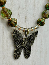 Load image into Gallery viewer, This intricately crafted pendant features a basil leaf molded in brass and adorned with stunningly warm greens, blues, and gold tone beaded necklace. Its eye-catching butterfly design adds a bold, yet whimsical touch, making it an ideal choice for a summer look. This beaded necklace is crafted from a combination of brass floral beads with a subtle patina hue, champagne melon beads, and dark, faceted avocado green pressed glass beads.  Measurements: Necklace is 18 1/2” in length - pendant is 1” Height