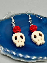 Load image into Gallery viewer, These stylish skull earrings are perfect for adding a unique flair to any outfit. Whether you're looking for a Dia De Los Muertos accessory or simply looking to draw inspiration, these goth pieces perfectly capture the vampire goth, witchy, dark, Chingona Cabrona, Latina Chicana styles. Howlite stone skull bead with red quartzize floral beads.  Measurements: 1 1/4 ” in length