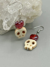 Load image into Gallery viewer, These stylish skull earrings are perfect for adding a unique flair to any outfit. Whether you're looking for a Dia De Los Muertos accessory or simply looking to draw inspiration, these goth pieces perfectly capture the vampire goth, witchy, dark, Chingona Cabrona, Latina Chicana styles. Howlite stone skull beaded earrings come with a ruby red heart-shaped glass beaded that has a very shimmery and vivid iridescent hue.  Measurements: 1 1/4 ” in length