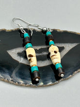Load image into Gallery viewer, These stylish skull earrings are perfect for adding a unique flair to any outfit. Whether you're looking for a Dia De Los Muertos accessory or simply looking to draw inspiration, these goth pieces perfectly capture the vampire goth, witchy, dark, Chingona Cabrona, Latina Chicana styles. Skull-shaped bone beads adorned with dark brown, turquoise, and gold beaded earrings make up this unique set of earrings. Measurements: 1 1/2 ” in length