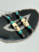 Load image into Gallery viewer, These stylish skull earrings are perfect for adding a unique flair to any outfit. Whether you're looking for a Dia De Los Muertos accessory or simply looking to draw inspiration, these goth pieces perfectly capture the vampire goth, witchy, dark, Chingona Cabrona, Latina Chicana styles. Skull-shaped bone beads adorned with dark brown, turquoise, and gold beaded earrings make up this unique set of earrings. Measurements: 1 1/2 ” in length