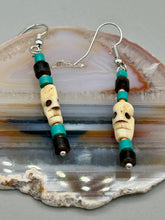 Load image into Gallery viewer, These stylish skull earrings are perfect for adding a unique flair to any outfit. Whether you're looking for a Dia De Los Muertos accessory or simply looking to draw inspiration, these goth pieces perfectly capture the vampire goth, witchy, dark, Chingona Cabrona, Latina Chicana styles. Skull-shaped bone beads adorned with dark brown, turquoise, and gold beaded earrings make up this unique set of earrings. Measurements: 1 1/2 ” in length