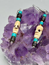 Load image into Gallery viewer, These stylish skull earrings are perfect for adding a unique flair to any outfit. Whether you're looking for a Dia De Los Muertos accessory or simply looking to draw inspiration, these goth pieces perfectly capture the vampire goth, witchy, dark, Chingona Cabrona, Latina Chicana styles. Skull-shaped bone beads adorned with dark brown, turquoise, and gold beaded earrings make up this unique set of earrings. Measurements: 1 1/2 ” in length