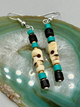 Load image into Gallery viewer, These stylish skull earrings are perfect for adding a unique flair to any outfit. Whether you're looking for a Dia De Los Muertos accessory or simply looking to draw inspiration, these goth pieces perfectly capture the vampire goth, witchy, dark, Chingona Cabrona, Latina Chicana styles. Skull-shaped bone beads adorned with dark brown, turquoise, and gold beaded earrings make up this unique set of earrings. Measurements: 1 1/2 ” in length