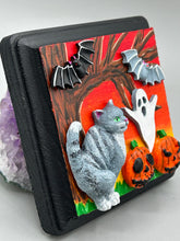 Load image into Gallery viewer, This handcrafted Halloween theme polymer clay wall art boasts a square-shaped wood frame with hand sculpted gray tabby cat, gray and black bats, jack-o-lantern and ghost motifs. Its warm sky hues, including yellow, to orange to dark red are further complemented by the black frame adding an extra layer of sophistication to the spooky warm-toned artwork.  Measurements: H 4" x W 4” x D 1 1/2"