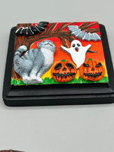 Load image into Gallery viewer, This handcrafted Halloween theme polymer clay wall art boasts a square-shaped wood frame with hand sculpted gray tabby cat, gray and black bats, jack-o-lantern and ghost motifs. Its warm sky hues, including yellow, to orange to dark red are further complemented by the black frame adding an extra layer of sophistication to the spooky warm-toned artwork.  Measurements: H 4" x W 4” x D 1 1/2"