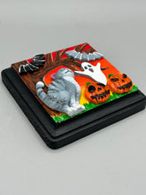Load image into Gallery viewer, This handcrafted Halloween theme polymer clay wall art boasts a square-shaped wood frame with hand sculpted gray tabby cat, gray and black bats, jack-o-lantern and ghost motifs. Its warm sky hues, including yellow, to orange to dark red are further complemented by the black frame adding an extra layer of sophistication to the spooky warm-toned artwork.  Measurements: H 4" x W 4” x D 1 1/2"