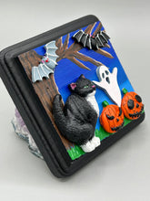 Load image into Gallery viewer, This handcrafted Halloween theme polymer clay wall art boasts a square-shaped wood frame with hand sculpted tuxedo cat, gray and black bats, jack-o-lantern and ghost motifs. Its cool sky hues, including light to dark blues are further complemented by the black frame adding an extra layer of sophistication to the spooky cool-toned artwork.  Measurements: H 4" x W 4” x D 1 1/2"