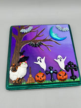 Load image into Gallery viewer, This captivating starry night calico kitty in the cemetery is artfully crafted with a black wood frame with a green iridescent finish and a dark purple hue background for an eye-catching and captivating nocturnal effect art piece. This kitty cat is dressed in a witch's hat while paying a visit to the cemetery accompanied by a broom and a jack-o-lantern and bat friends. This bewitching and whimsical Halloween-themed art piece adds a one-of-a-kind Halloween touch to any home or office.