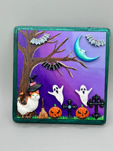 Load image into Gallery viewer, This captivating starry night calico kitty in the cemetery is artfully crafted with a black wood frame with a green iridescent finish and a dark purple hue background for an eye-catching and captivating nocturnal effect art piece. This kitty cat is dressed in a witch's hat while paying a visit to the cemetery accompanied by a broom and a jack-o-lantern and bat friends. This bewitching and whimsical Halloween-themed art piece adds a one-of-a-kind Halloween touch to any home or office.