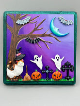 Load image into Gallery viewer, This captivating starry night calico kitty in the cemetery is artfully crafted with a black wood frame with a green iridescent finish and a dark purple hue background for an eye-catching and captivating nocturnal effect art piece. This kitty cat is dressed in a witch's hat while paying a visit to the cemetery accompanied by a broom and a jack-o-lantern and bat friends. This bewitching and whimsical Halloween-themed art piece adds a one-of-a-kind Halloween touch to any home or office.