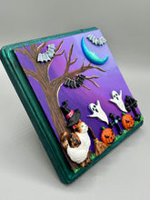 Load image into Gallery viewer, This captivating starry night calico kitty in the cemetery is artfully crafted with a black wood frame with a green iridescent finish and a dark purple hue background for an eye-catching and captivating nocturnal effect art piece. This kitty cat is dressed in a witch's hat while paying a visit to the cemetery accompanied by a broom and a jack-o-lantern and bat friends. This bewitching and whimsical Halloween-themed art piece adds a one-of-a-kind Halloween touch to any home or office.