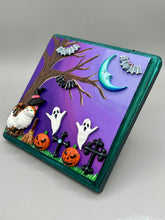 Load image into Gallery viewer, This captivating starry night calico kitty in the cemetery is artfully crafted with a black wood frame with a green iridescent finish and a dark purple hue background for an eye-catching and captivating nocturnal effect art piece. This kitty cat is dressed in a witch's hat while paying a visit to the cemetery accompanied by a broom and a jack-o-lantern and bat friends. This bewitching and whimsical Halloween-themed art piece adds a one-of-a-kind Halloween touch to any home or office.