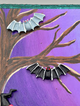 Load image into Gallery viewer, This captivating starry night calico kitty in the cemetery is artfully crafted with a black wood frame with a green iridescent finish and a dark purple hue background for an eye-catching and captivating nocturnal effect art piece. This kitty cat is dressed in a witch's hat while paying a visit to the cemetery accompanied by a broom and a jack-o-lantern and bat friends. This bewitching and whimsical Halloween-themed art piece adds a one-of-a-kind Halloween touch to any home or office.