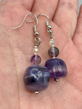 Load image into Gallery viewer, This luxurious set of earrings feature large square-shaped rainbow fluorite beads contrasted against round amethyst beads, presenting an elegant neutral yet cool-toned look. With its unique and versatile style, these earrings make a perfect addition to any wardrobe. Measurements: 1 3/8” in length