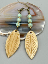 Load image into Gallery viewer, Single-stranded earring features bone carved leaf charm earrings with light mint green melon Czech faceted round glass beads.  Glass beads have a tint of light gold shimmer. Antique antique brass plated steel ear-wire French Hook Earrings.   Measurements: 3” in length