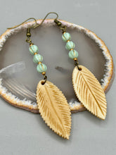 Load image into Gallery viewer, Single-stranded earring features bone carved leaf charm earrings with light mint green melon Czech faceted round glass beads.  Glass beads have a tint of light gold shimmer. Antique antique brass plated steel ear-wire French Hook Earrings.   Measurements: 3” in length