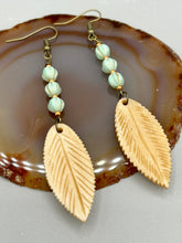 Load image into Gallery viewer, Single-stranded earring features bone carved leaf charm earrings with light mint green melon Czech faceted round glass beads.  Glass beads have a tint of light gold shimmer. Antique antique brass plated steel ear-wire French Hook Earrings.   Measurements: 3” in length