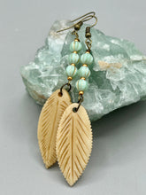 Load image into Gallery viewer, Single-stranded earring features bone carved leaf charm earrings with light mint green melon Czech faceted round glass beads.  Glass beads have a tint of light gold shimmer. Antique antique brass plated steel ear-wire French Hook Earrings.   Measurements: 3” in length