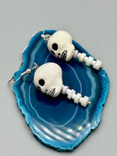 Load image into Gallery viewer, Peruvian off white ceramic skull beads come with spine earrings. These stylish skull earrings are perfect for adding a unique flair to any outfit. Whether you're looking for a Dia De Los Muertos accessory or simply looking to draw inspiration, these goth pieces perfectly capture the vampire goth, witchy, dark, Chingona Cabrona, Latina Chicana styles. Measurements: 1 1/4” in length