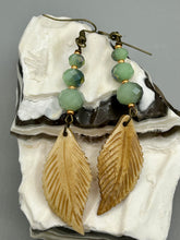 Load image into Gallery viewer, Single-stranded earring features bone carved leaf charm earrings with light mint faceted round glass beads.  Glass beads have a tint of dark green and gold shimmer. Antique antique brass plated steel ear-wire French Hook Earrings.   Measurements: 3” in length