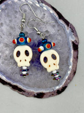 Load image into Gallery viewer, Spooky but festive skull beads with hematite bead spines and come with fiesta shaped crown glass earrings. These stylish skull earrings are perfect for adding a unique flair to any outfit. Whether you're looking for a Dia De Los Muertos accessory or simply looking to draw inspiration, these goth pieces perfectly capture the vampire goth, witchy, dark, Chingona Cabrona, Latina Chicana styles. Measurements: 1 1/2” in length