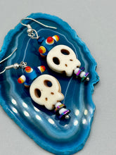 Load image into Gallery viewer, Spooky but festive skull beads with hematite bead spines and come with fiesta shaped crown glass earrings. These stylish skull earrings are perfect for adding a unique flair to any outfit. Whether you're looking for a Dia De Los Muertos accessory or simply looking to draw inspiration, these goth pieces perfectly capture the vampire goth, witchy, dark, Chingona Cabrona, Latina Chicana styles. Measurements: 1 1/2” in length