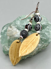 Load image into Gallery viewer, Single-stranded earring features bone carved leaf charm earrings with black and white swirly eye-dot glass beads. Antique Copper Plated Surgical Steel Hammered Long Ear-wire French Hook Earrings. Measurements: 3” in length