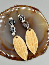 Load image into Gallery viewer, Single-stranded earring features bone carved leaf charm earrings with black and white swirly eye-dot glass beads. Antique Copper Plated Surgical Steel Hammered Long Ear-wire French Hook Earrings. Measurements: 3” in length