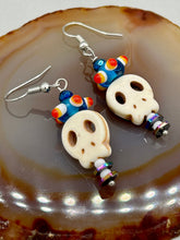 Load image into Gallery viewer, Spooky but festive skull beads with hematite bead spines and come with fiesta shaped crown glass earrings. These stylish skull earrings are perfect for adding a unique flair to any outfit. Whether you're looking for a Dia De Los Muertos accessory or simply looking to draw inspiration, these goth pieces perfectly capture the vampire goth, witchy, dark, Chingona Cabrona, Latina Chicana styles. Measurements: 1 1/2” in length