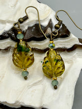 Load image into Gallery viewer, This pair of earrings features a dark amber and green tone, pressed glass leaf charm in an iridescent finish that gives off subtle hues of gold. Complemented with light ming green glass beaded earrings, this set is sure to sparkle.   Measurements: 1 1/4" length