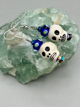 Load image into Gallery viewer, Spooky but festive Peruvian ceramic skull beads with hematite beaded spines and come with fiesta shaped crown glass earrings. These stylish skull earrings are perfect for adding a unique flair to any outfit. Whether you're looking for a Dia De Los Muertos accessory or simply looking to draw inspiration, these goth pieces perfectly capture the vampire goth, witchy, dark, Chingona Cabrona, Latina Chicana styles. Measurements: 1 1/4” in length