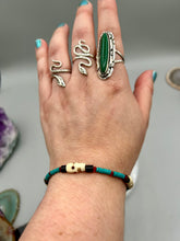 Load image into Gallery viewer, These stylish skull bracelet is perfect for adding a unique flair to any outfit. Whether you're looking for a Dia De Los Muertos accessory or simply looking to draw inspiration, these goth pieces perfectly capture the vampire goth, witchy, dark, Chingona Cabrona, Latina Chicana styles. Skull-shaped bone beads adorned with dark brown, turquoise, and gold beads make up this unique statement piece. Measurements: Bracelet: 7 1/2"