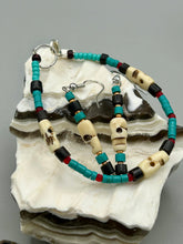 Load image into Gallery viewer, These stylish skull earrings are perfect for adding a unique flair to any outfit. Whether you're looking for a Dia De Los Muertos accessory or simply looking to draw inspiration, these goth pieces perfectly capture the vampire goth, witchy, dark, Chingona Cabrona, Latina Chicana styles. Skull-shaped bone beads adorned with dark brown, turquoise, and gold beaded earrings make up this unique set of earrings. Measurements: 1 1/2 ” in length